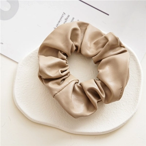 Close-up of khaki PU leather scrunchie on a white base with minimalist lighting