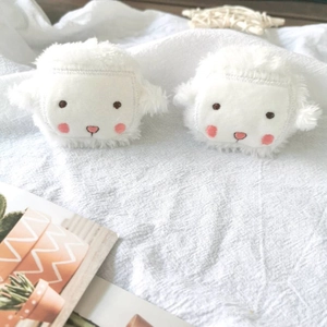 Close-up of cute plush lamb brooches with blush details on white textured background