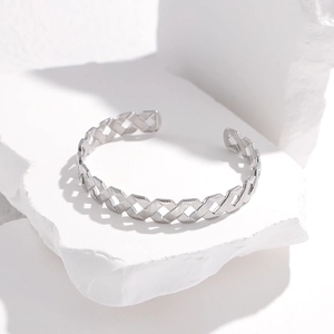 Detail shot of silver geometric lattice cutout bangle on white stone with side lighting