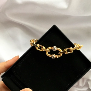 Macro detail of gold U-link chain bracelet with contrasting silver ball charm on box