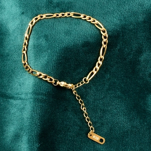 Primer plano de pulsera Figaro de oro de 18 quilates con placa K18 sobre terciopelo verde