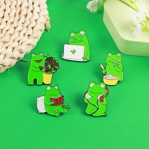 Set of five cute green frog enamel pins showing daily life activities like reading and baking