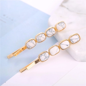 Pair of gold hair clips with white marble square inlay on a minimalist light blue surface
