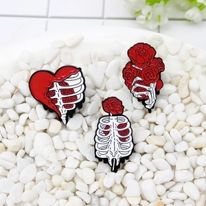 Gothic skull hands and ribcage pins with red roses on white stones background