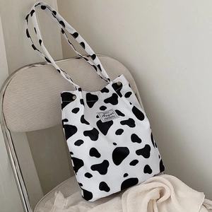 Detail of Augur canvas tote bag featuring black and white cow print and brand label