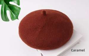 Dettaglio di un basco in lana color caramello per bambini su un libro con foglie