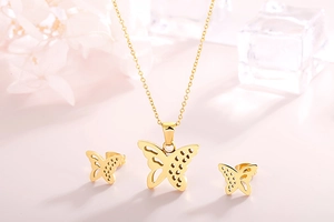 Elegant gold-tone butterfly necklace and stud earrings set on a soft pink background