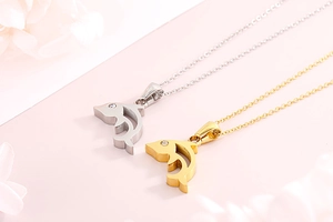 Detail view of gold and silver fish necklaces with crystal eyes on a pink background