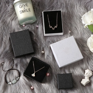 Flat lay of black and white jewelry boxes with necklaces on luxury grey plush fabric