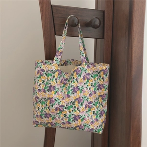 Detail of floral canvas tote bag with purple and yellow flower prints hanging on a rack