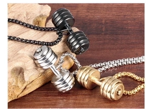 Three dumbbell pendants in black, silver, and gold on box chains over dark wood background