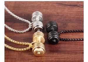 Three dumbbell pendants in silver, gold, and black steel on dark wood background