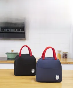 Detail of insulated lunch bags with red handles and round logos on a wooden table