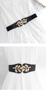 Detail of black elastic belt with golden leaf metal buckle on white dress