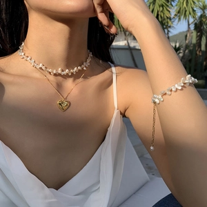 Detail of baroque pearl necklace and gold chain bracelet set with a heart pendant