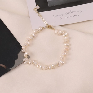 Detail of baroque pearl bracelet with gold lobster clasp on beige textured background