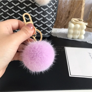 Detailed view of a soft purple fur ball keychain with a gold lobster clasp on a bag