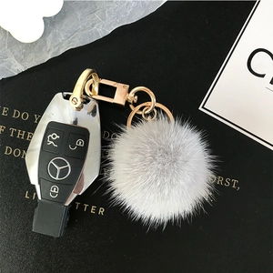 Close-up of soft light grey mink fur ball keychain attached to a car key with gold hardware