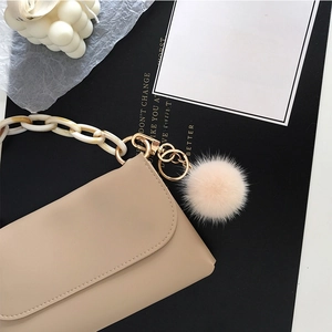 Detail of soft beige fur ball keychain on handbag with chic acrylic marble chain