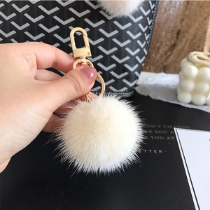 Close-up of white fluffy fur pompom keychain with gold metal clasp on a textured handbag