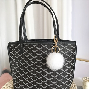 Detail of a white faux fur pompom charm attached to a black patterned tote bag