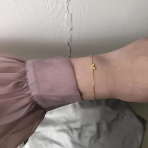 Minimalist gold heart charm bracelet in stainless steel worn on wrist with purple sleeve