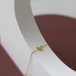 Detailed close-up of a golden heart pendant on a thin chain over geometric props