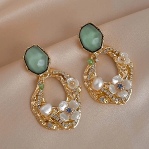 Detailed shot of vintage baroque earrings with green stones and pearls on silk fabric
