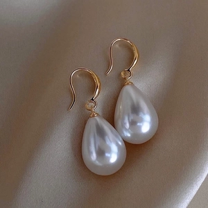 Macro shot of French vintage teardrop pearl earrings with gold hooks on silk background