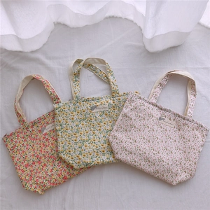 Détail de trois sacs cabas en coton à fleurs avec étiquettes sur tissu blanc plissé