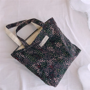 Détail du sac cabas en toile à motif floral noir avec des anses en coton blanc cassé