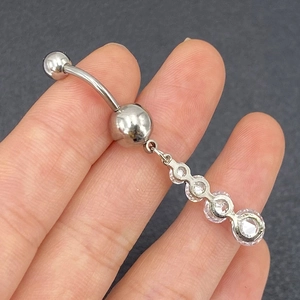 Macro detail of silver stainless steel belly button ring with four round clear zircons