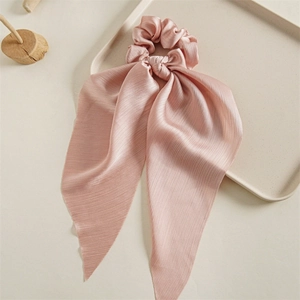Close-up of pink satin scrunchie with long ribbons on a minimalist wood display
