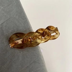 Detail of amber resin chain hair clip with polished gold metal base on stone surface