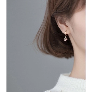 Close-up of a pink cherry earring with gold stem and green leaf on woman ear