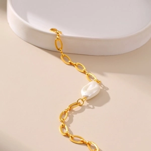 Macro detail of golden textured chain link and a single luminous baroque pearl on the bracelet