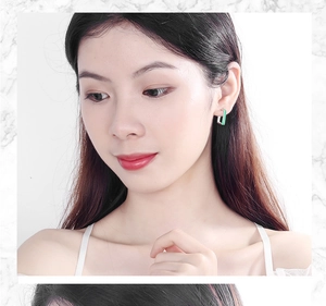 Detail view of a model wearing minimalist silver square stud earrings with green enamel inlay