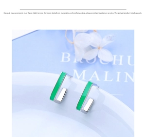 Detail of square J-shaped silver earrings with green enamel on a clean backdrop