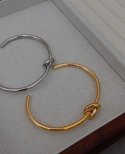 Detailed top view of gold and silver knot open bangles inside a beige jewelry gift box
