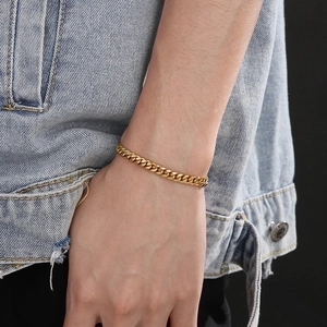 Hip hop style gold stainless steel Cuban link bracelet worn on wrist with denim jacket