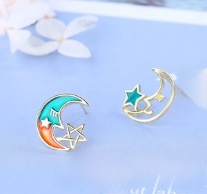 Close-up of star and moon stud earrings with colorful enamel on a light blue background