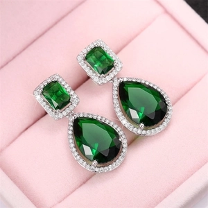 Elegant silver drop earrings with pear-cut emerald green zircons on pink velvet