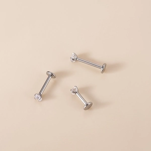 Detailed view of three G23 titanium labret studs with zircon crystals on beige background