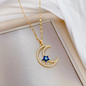 Golden star and moon necklace with clear crystals and blue evil eye on white silk