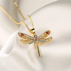 Macro shot of gold dragonfly pendant with colorful zircon stones on white silk fabric