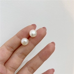 Close-up of small natural freshwater pearl earrings held between fingers for scale