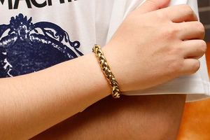Gros plan d'un bracelet pour homme en chaîne de dragon dorée porté sur le poignet en blanc