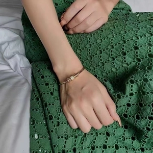 Detail of rose gold open bangle with pavé crystal cylinder worn on hand with lace background