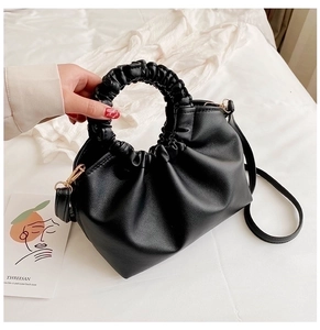 Detail of black pleated handbag featuring ruffled handle and shiny faux leather texture