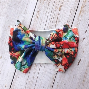 Detailed view of floral baby headband with large bow on a white wood texture background